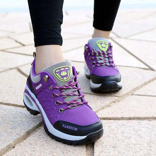 Scarpe da ginnastica viola da donna su pavimento in pietra, design moderno con suola robusta, dettagli neri e grigi, ideali per sport e tempo libero.