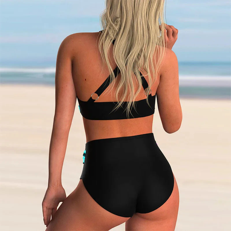 Donna in bikini nero a vita alta su spiaggia sabbiosa, capelli biondi sciolti, mare sullo sfondo. Moda mare, costumi da bagno eleganti.