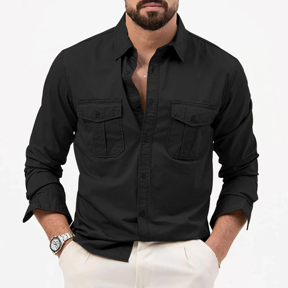 Camicia nera da uomo con tasche frontali, maniche lunghe arrotolate, abbinata a pantaloni chiari. Stile casual elegante, moda maschile.