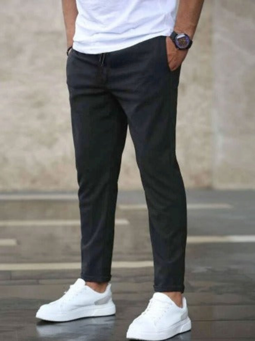 Uomo in pantaloni neri e scarpe da ginnastica bianche, mani in tasca, sfondo urbano. Moda casual maschile, stile moderno, abbigliamento quotidiano.
