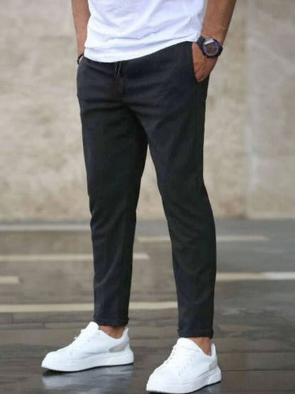 Uomo in pantaloni neri e scarpe da ginnastica bianche, mani in tasca, sfondo urbano. Moda casual maschile, stile moderno, abbigliamento quotidiano.