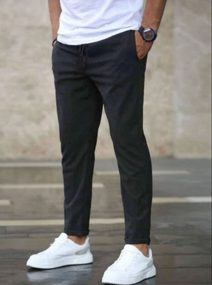 Uomo in pantaloni chino neri e scarpe da ginnastica bianche, indossa una maglietta bianca. Stile casual maschile, moda urbana.