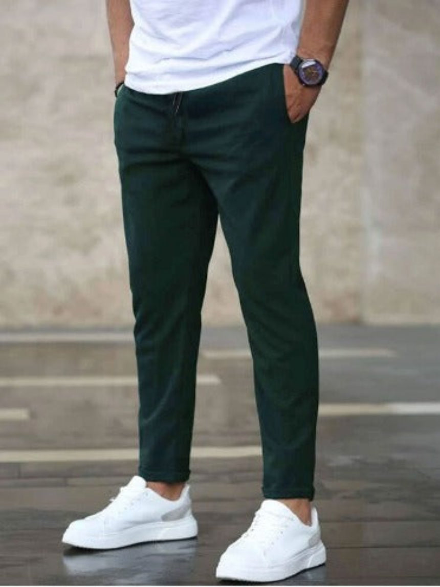 Uomo con pantaloni verde scuro, t-shirt bianca e scarpe da ginnastica bianche. Moda casual maschile, stile urbano, abbigliamento moderno.