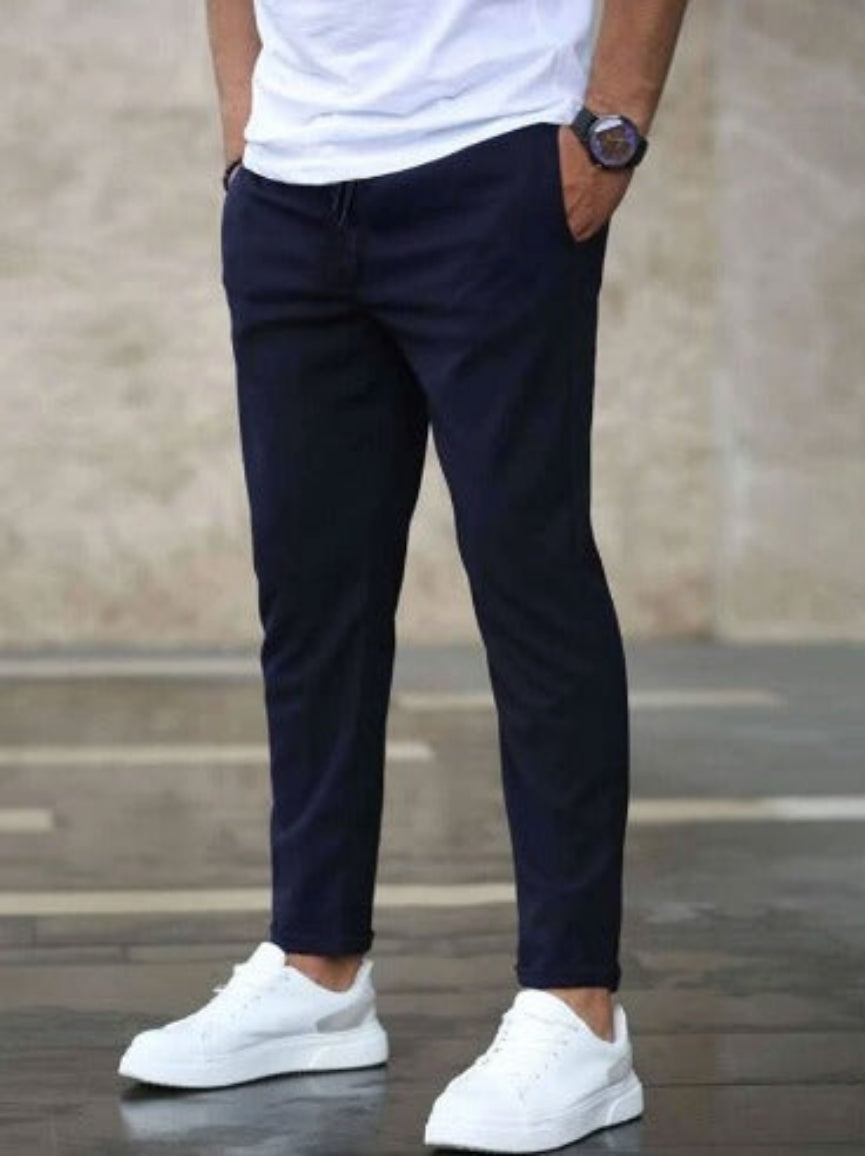 Uomo con pantaloni blu scuro e scarpe da ginnastica bianche, indossa una maglietta bianca. Stile casual elegante, moda maschile moderna.