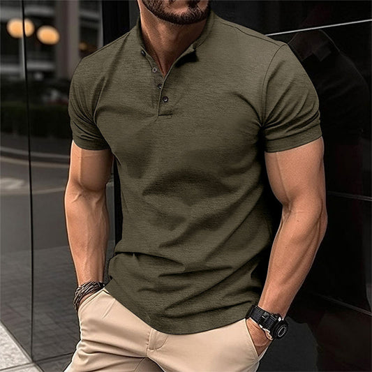Uomo in polo verde oliva, muscoloso, indossa pantaloni beige, orologio nero e bracciali, in contesto urbano. Moda maschile casual elegante.