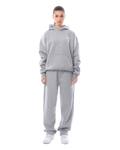 Donna in tuta grigia con cappuccio, pantaloni larghi e scarpe bianche. Abbigliamento casual, moda streetwear, comfort quotidiano.