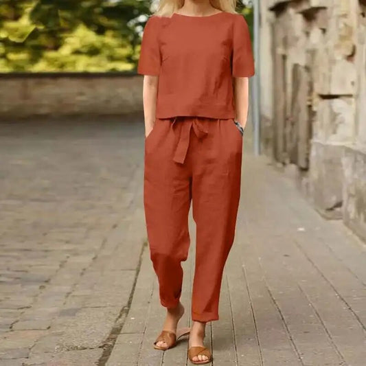 Donna con completo estivo arancione, pantaloni e maglietta coordinati, cammina su strada lastricata. Moda casual, abbigliamento estivo donna.