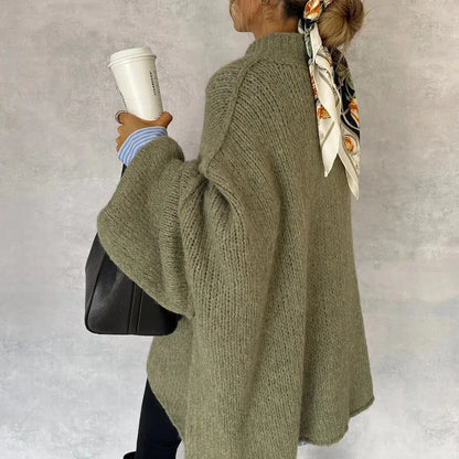 Donna di spalle con maglione oversize verde, capelli raccolti con foulard, tiene caffè da asporto e borsa nera. Moda autunnale casual.