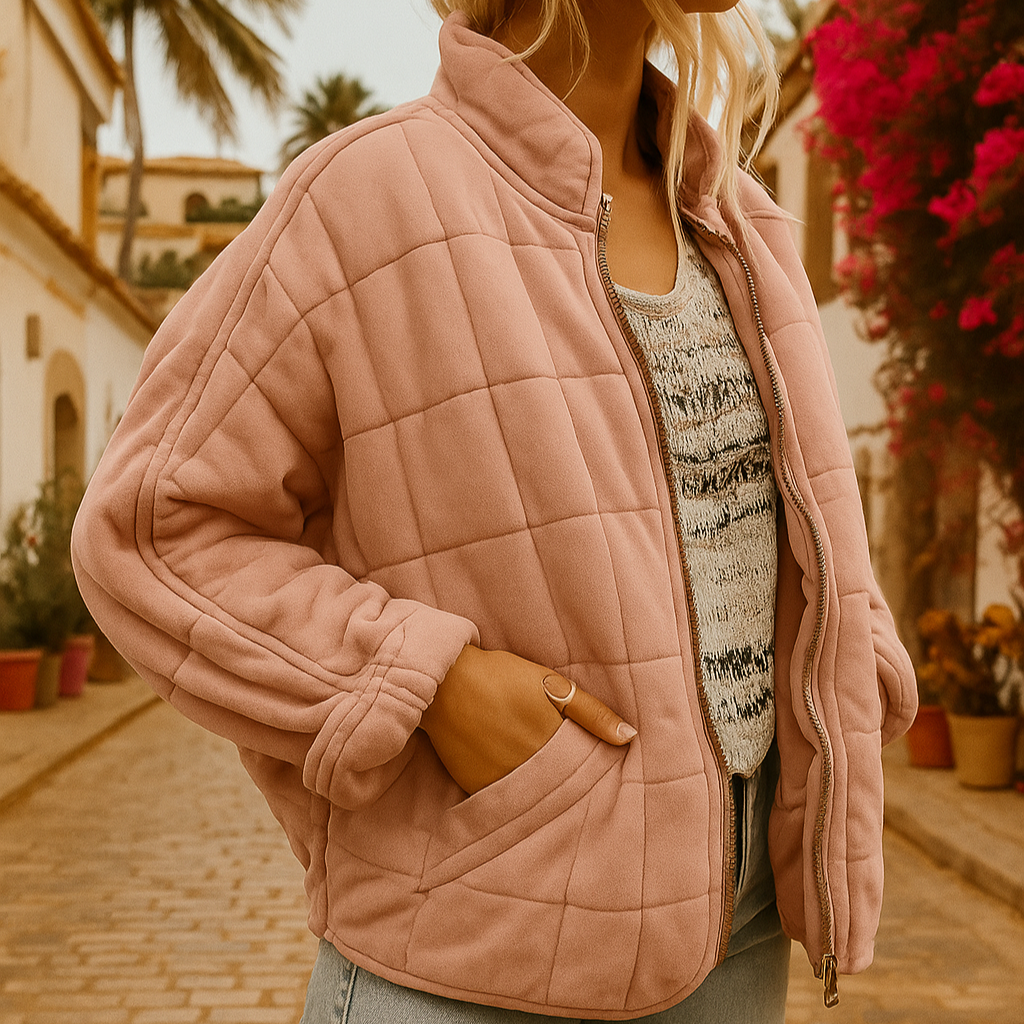 Giacca trapuntata rosa su donna in strada mediterranea, fiori vivaci e palme sullo sfondo. Moda autunnale, stile casual chic.
