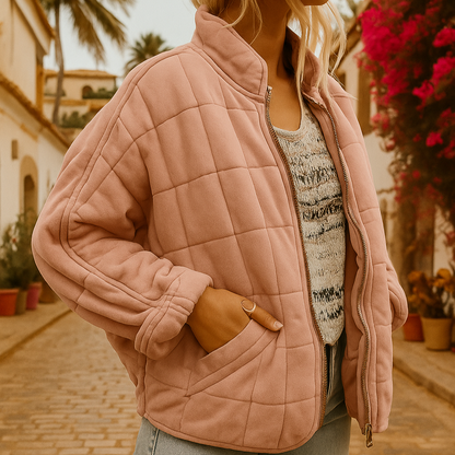 Giacca trapuntata rosa su donna in strada mediterranea, fiori vivaci e palme sullo sfondo. Moda autunnale, stile casual chic.