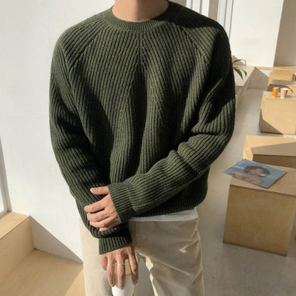 Maglione verde scuro a coste indossato da una persona in piedi, illuminato dalla luce naturale. Stile casual, perfetto per l'autunno e l'inverno.