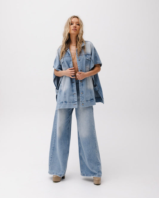 Donna in posa con abbigliamento in denim, giacca oversize e pantaloni a zampa, su sfondo bianco. Moda casual, stile anni '90, tendenze denim.