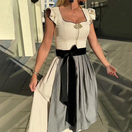 Donna in abito tradizionale dirndl con corpetto bianco e gonna a pieghe grigia, cintura nera, all'aperto in una giornata soleggiata.