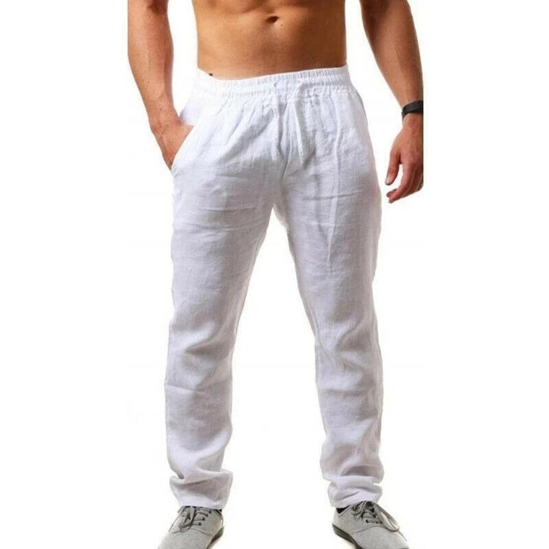 Uomo in pantaloni di lino bianchi, elastico in vita, mani in tasca, scarpe sportive grigie. Moda estiva casual maschile.