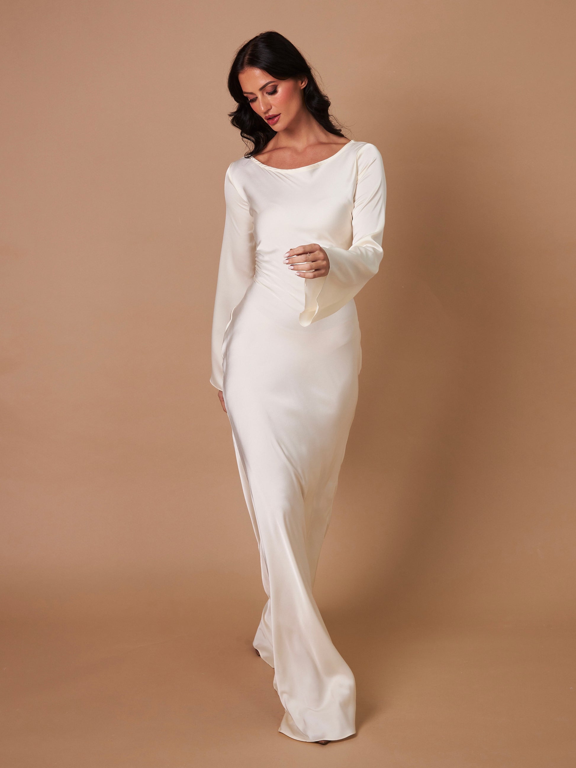 Donna in abito da sposa bianco elegante, maniche lunghe, su sfondo beige. Moda nuziale, abito da cerimonia, stile classico.