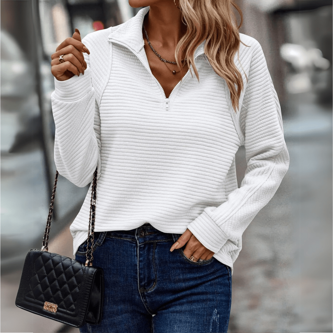 Donna con maglione bianco a coste, jeans blu e borsa nera trapuntata. Moda autunnale, stile casual chic, abbigliamento femminile elegante.
