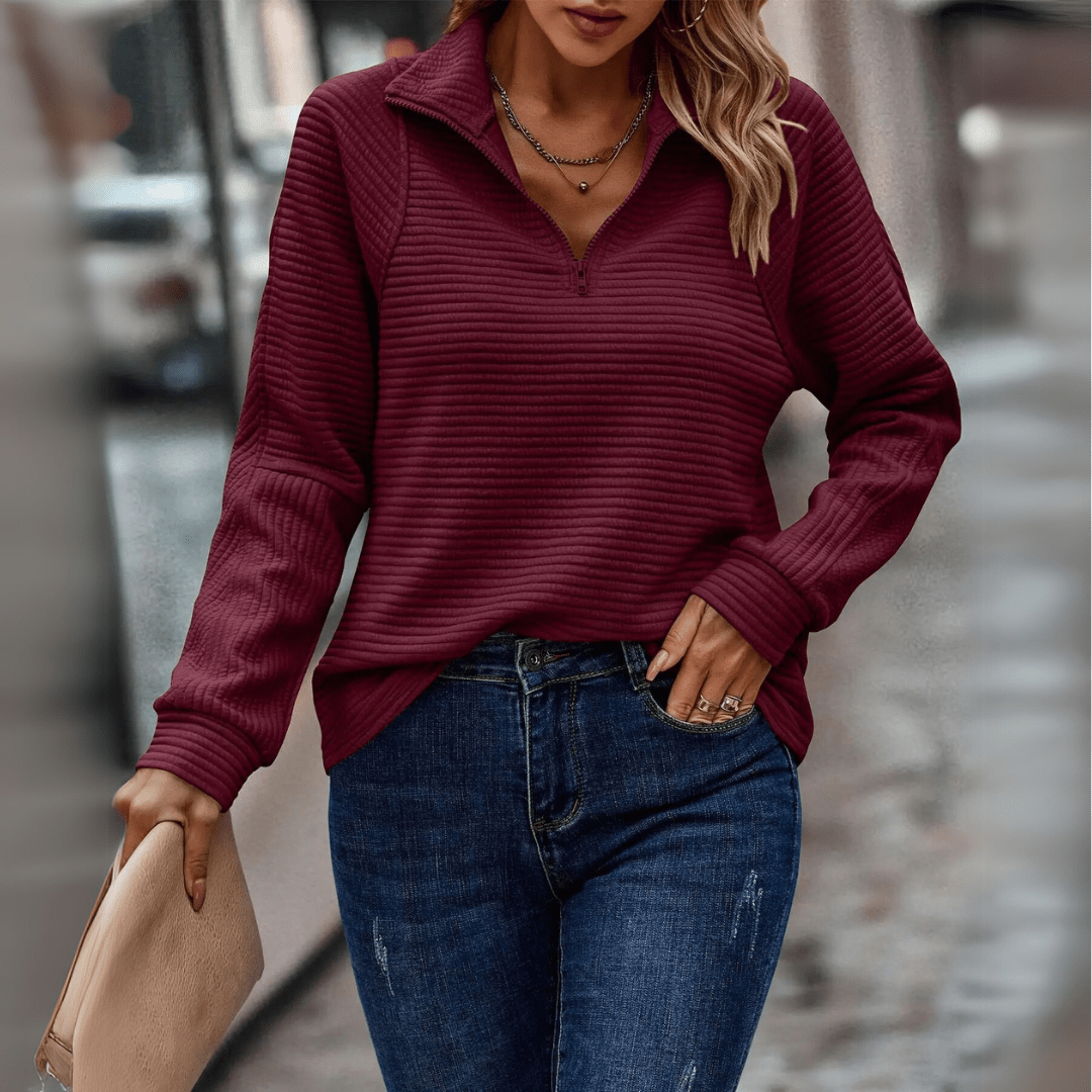 Donna con maglione bordeaux a coste e jeans blu, tiene una borsa beige. Moda autunnale casual, abbigliamento femminile elegante in città.
