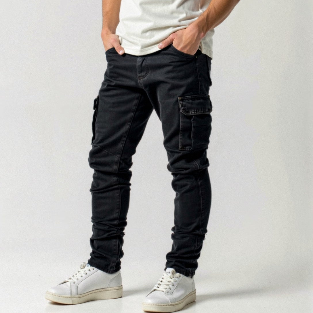 Jeans cargo neri da uomo con tasche laterali, abbinati a scarpe da ginnastica bianche e maglietta bianca. Moda casual maschile moderna.