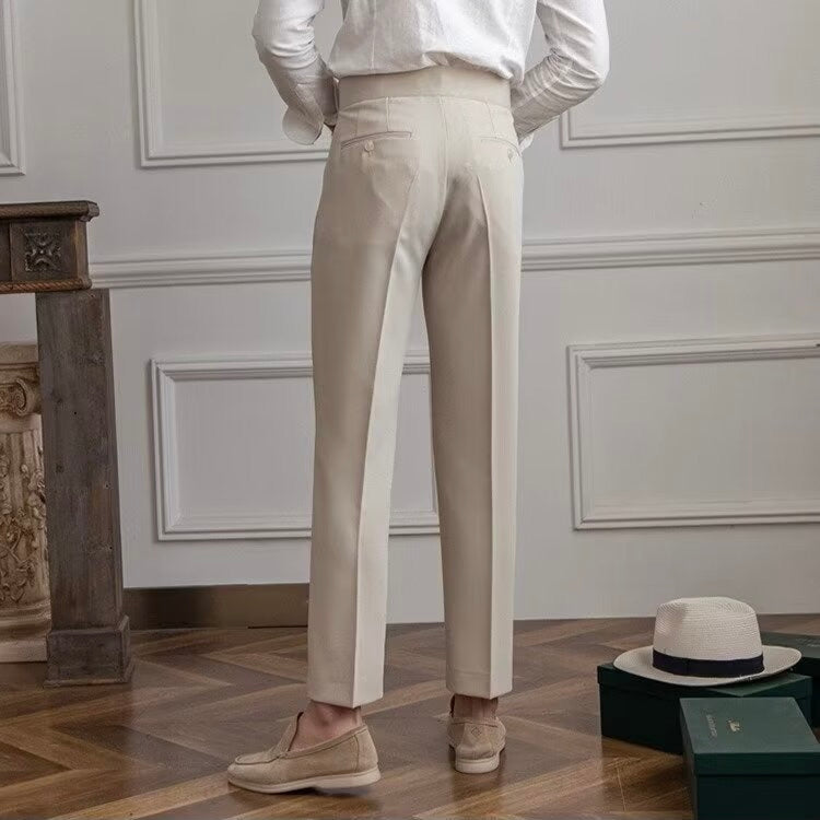 Uomo in pantaloni beige eleganti, camicia bianca, mocassini, in un interno classico con pavimento in legno e cappello Panama. Moda maschile sofisticata.