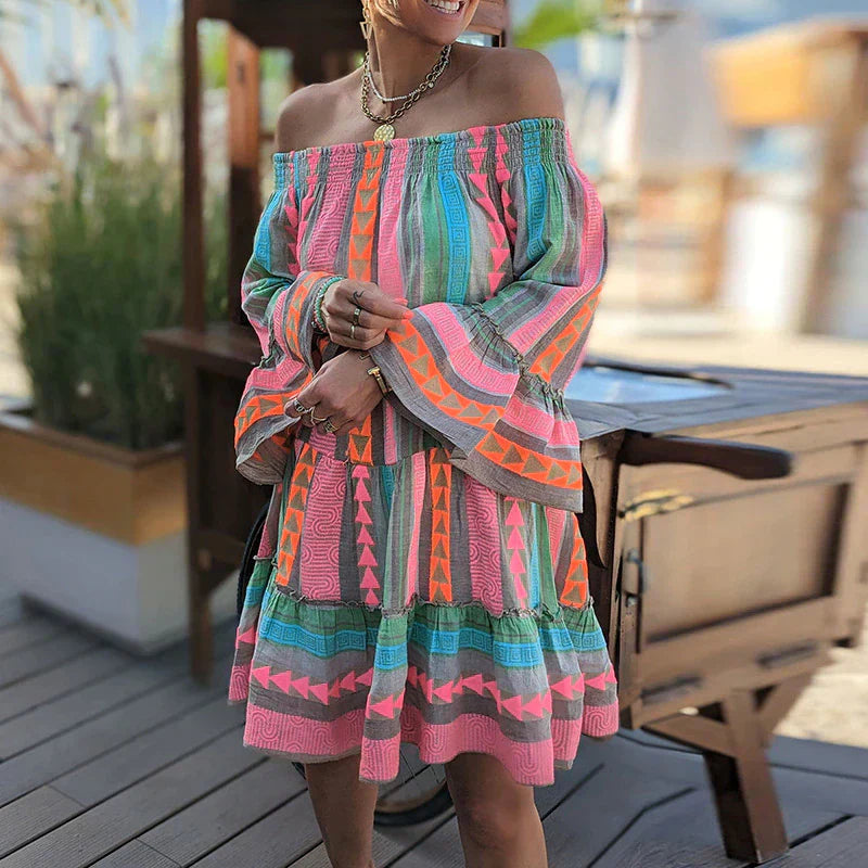 Abito estivo colorato con motivi geometrici, maniche lunghe e scollo a barca, indossato da una donna all'aperto. Moda estiva, abbigliamento casual.