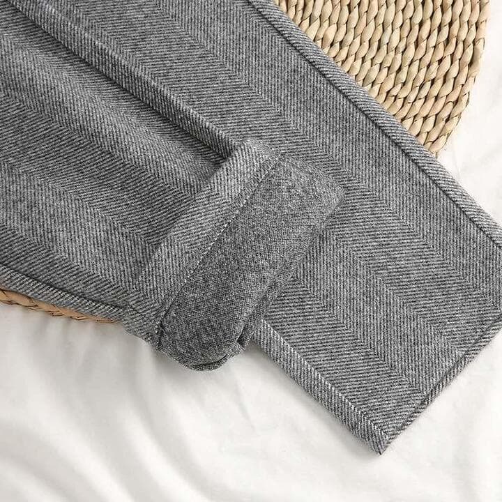 Pantaloni grigi in tessuto a spina di pesce, piegati su un tappetino intrecciato. Stile elegante, moda autunno-inverno, abbigliamento uomo.