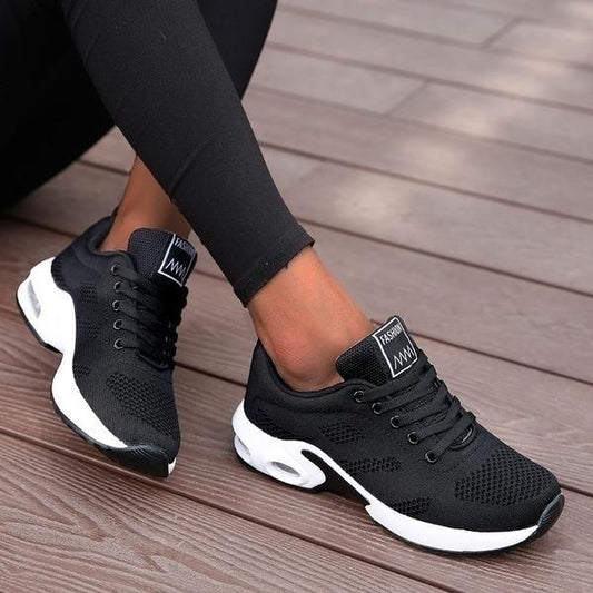 Scarpe da ginnastica nere su pavimento in legno, design moderno e traspirante, ideali per sport e tempo libero. Scarpe comode e alla moda.