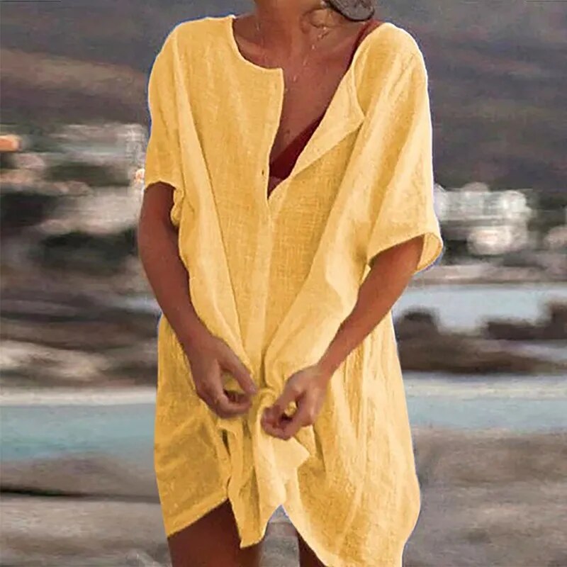 Donna in spiaggia con copricostume giallo in lino, sfondo marino sfocato. Abbigliamento estivo, moda mare, look casual.