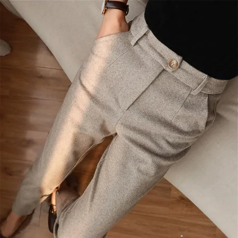 Pantaloni eleganti da donna in tessuto grigio chiaro, stile formale, con tasche laterali e cintura, indossati con maglia nera.