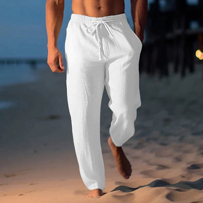 Uomo in pantaloni di lino bianchi cammina sulla spiaggia al tramonto. Abbigliamento estivo, moda maschile, relax in riva al mare.