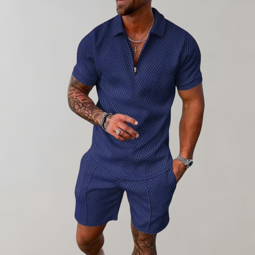 Uomo con tuta estiva blu a motivi geometrici, maniche corte, collana e bracciali. Moda maschile casual, abbigliamento estivo elegante.