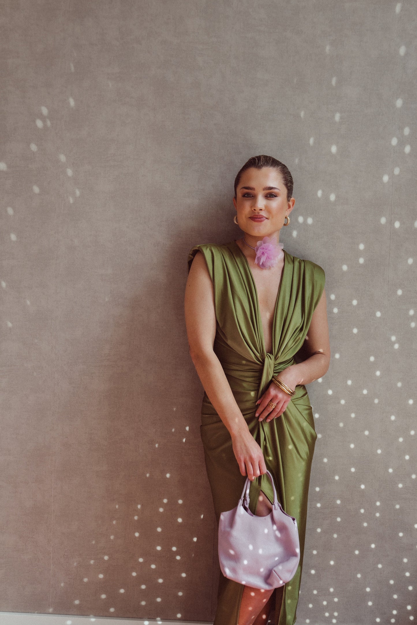 Donna in abito verde elegante con borsa rosa, sfondo grigio con riflessi luminosi. Moda femminile, stile sofisticato, accessori di tendenza.