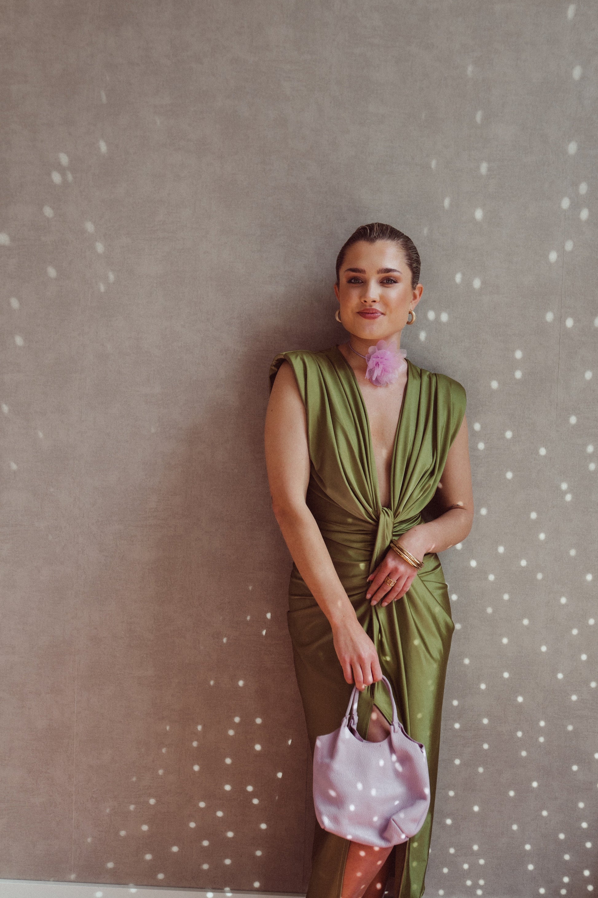 Donna in abito verde elegante con borsa rosa, sfondo grigio con riflessi luminosi. Moda femminile, stile sofisticato, accessori di tendenza.