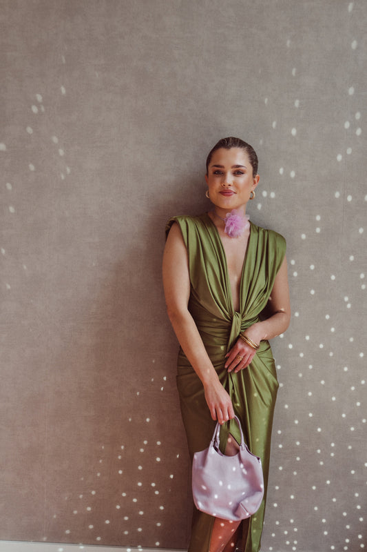 Donna in abito verde elegante con borsa rosa, sfondo grigio con riflessi luminosi. Moda femminile, stile sofisticato, accessori di tendenza.