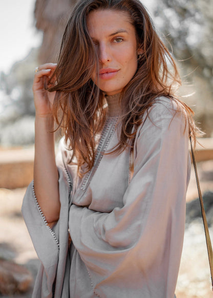 Donna con capelli castani sciolti indossa abito beige in stile boho-chic all'aperto, sfondo naturale sfocato. Moda femminile, look estivo elegante.