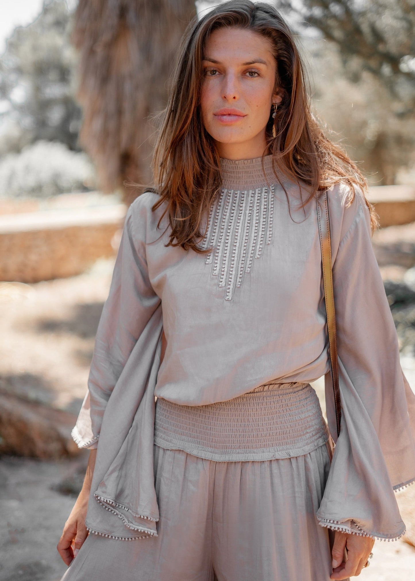 Donna con abito beige elegante, dettagli ricamati, in un ambiente naturale. Moda femminile, stile boho-chic, abbigliamento estivo.