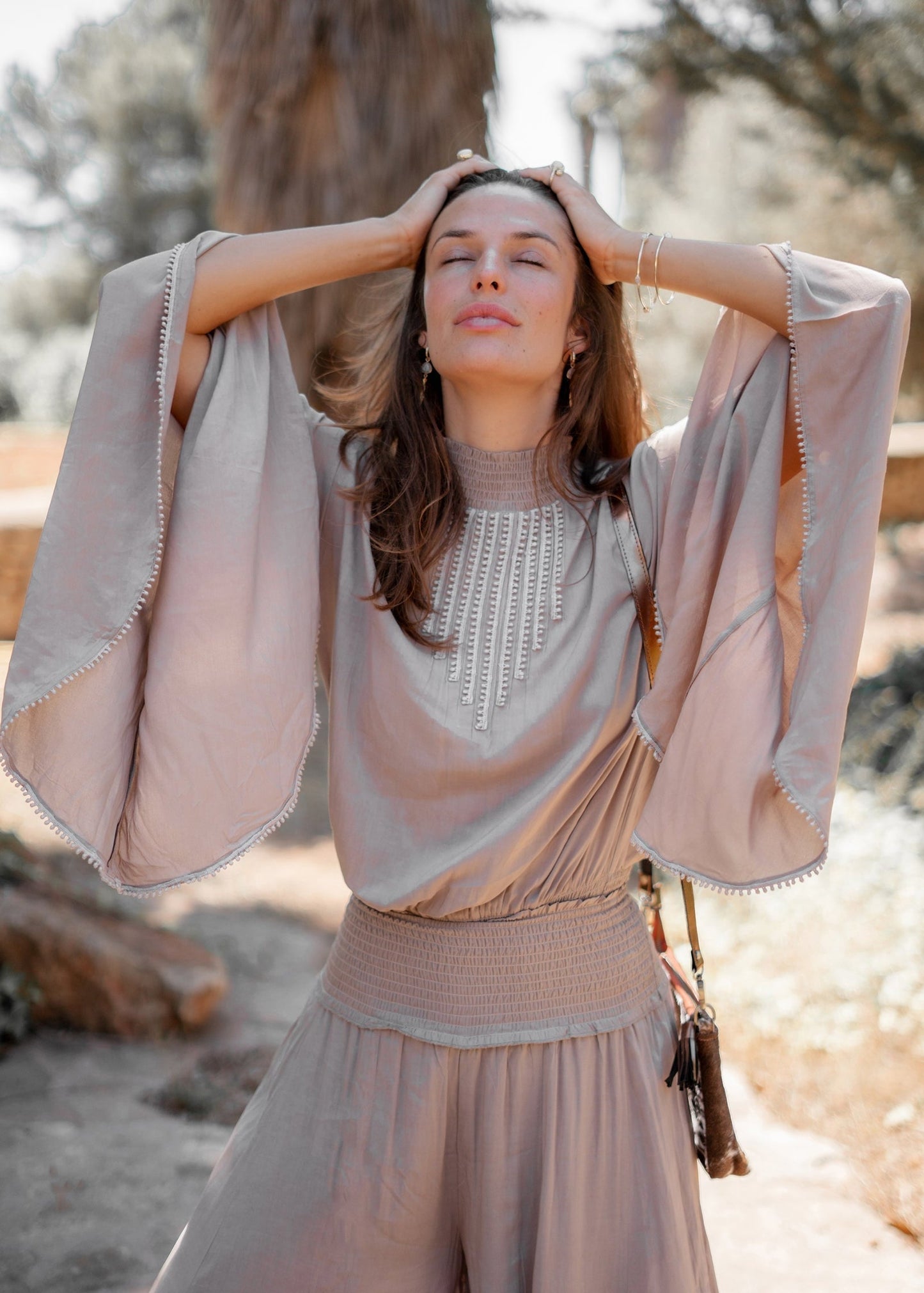 Donna in abito boho chic beige con maniche ampie, in posa rilassata all'aperto. Moda estiva, stile bohemien, tendenze abbigliamento femminile.