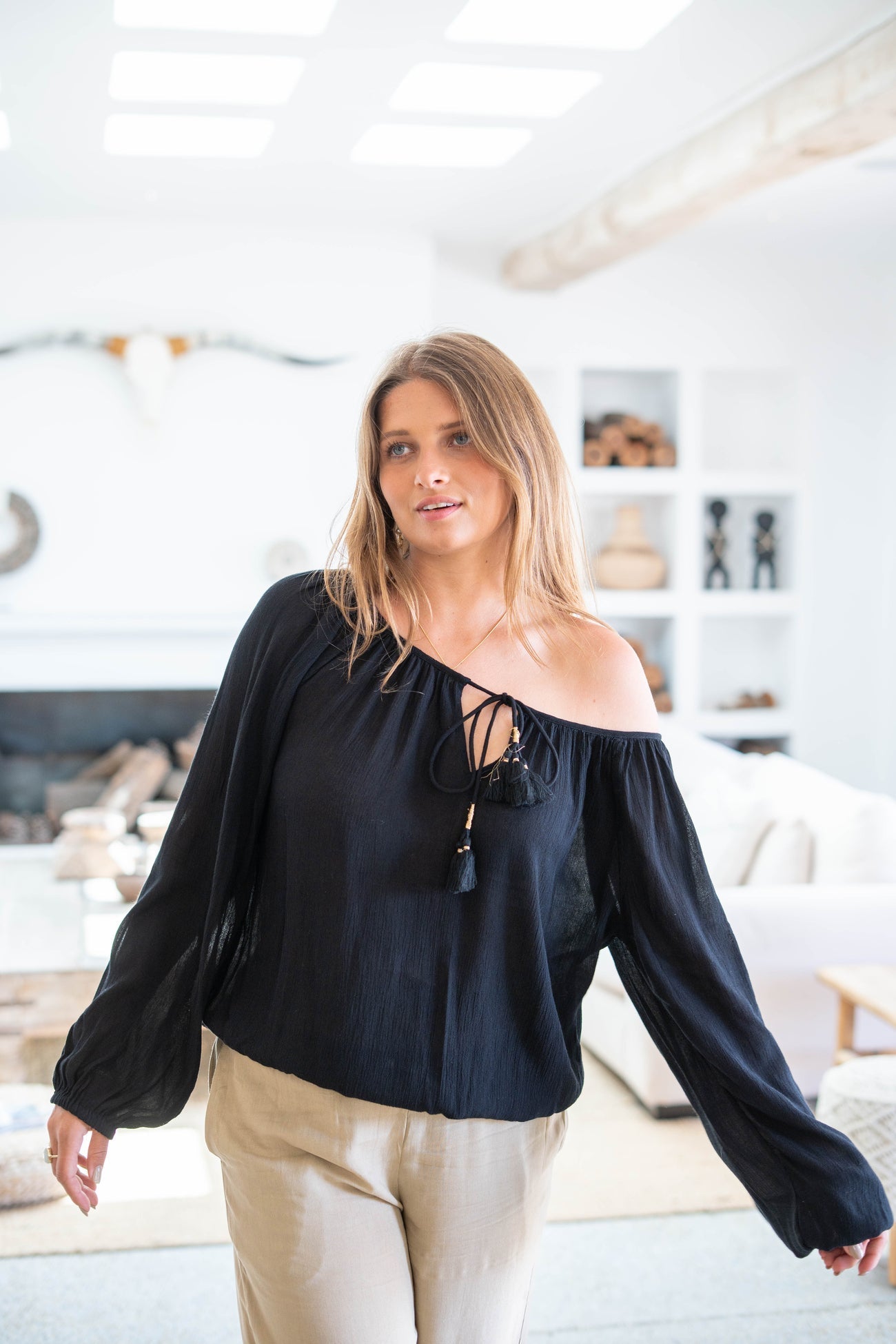 Donna con camicetta nera a spalle scoperte in soggiorno moderno, decorazione minimalista, luce naturale, arredamento elegante.