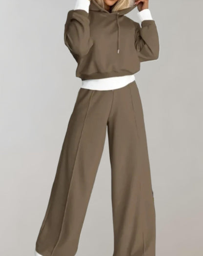 Donna in tuta sportiva marrone con cappuccio, pantaloni larghi e dettagli bianchi. Abbigliamento casual e comodo per moda autunnale.