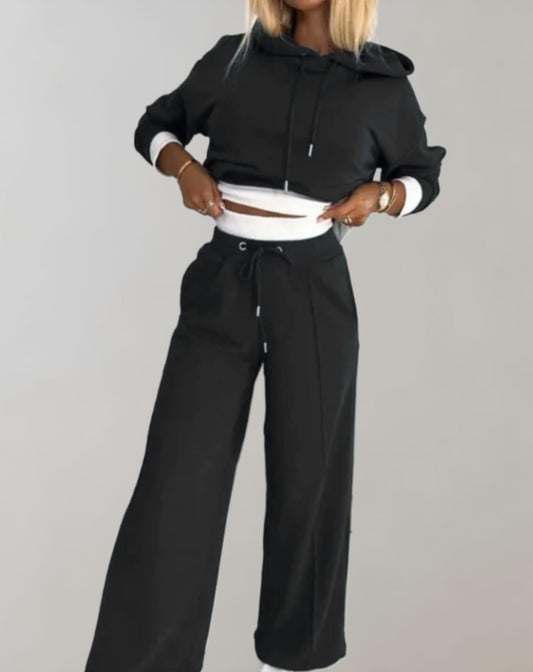 Donna in tuta nera con cappuccio, pantaloni larghi e dettagli bianchi. Moda casual, abbigliamento comodo, stile urbano.