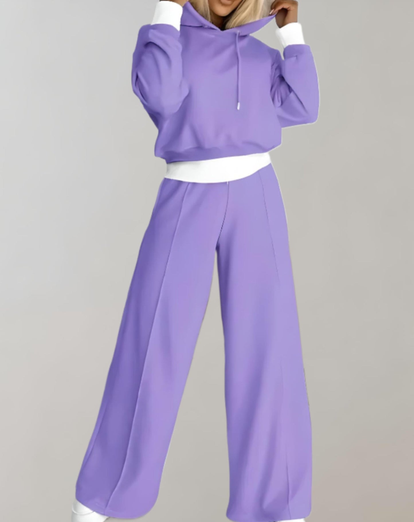 Donna in tuta sportiva viola, felpa con cappuccio e pantaloni larghi. Moda casual, abbigliamento comodo, stile moderno. Sfondo neutro.