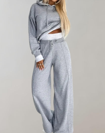 Donna in tuta grigia, felpa con cappuccio e pantaloni larghi, moda casual, abbigliamento sportivo, stile comodo, abbigliamento donna moderno.