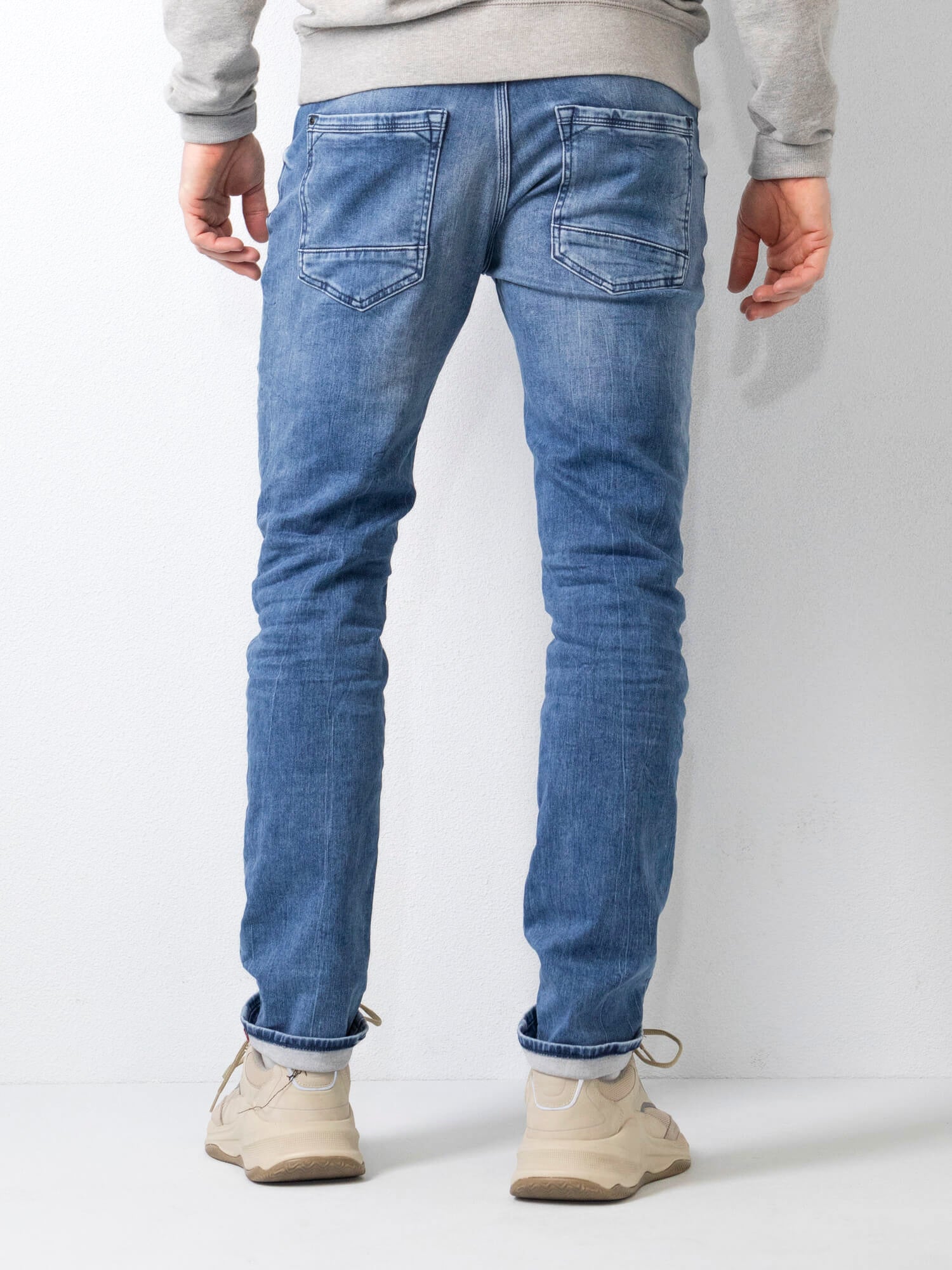 Jeans uomo slim fit blu chiaro, tasche posteriori, abbinati a scarpe beige e felpa grigia. Moda casual maschile, abbigliamento trendy.