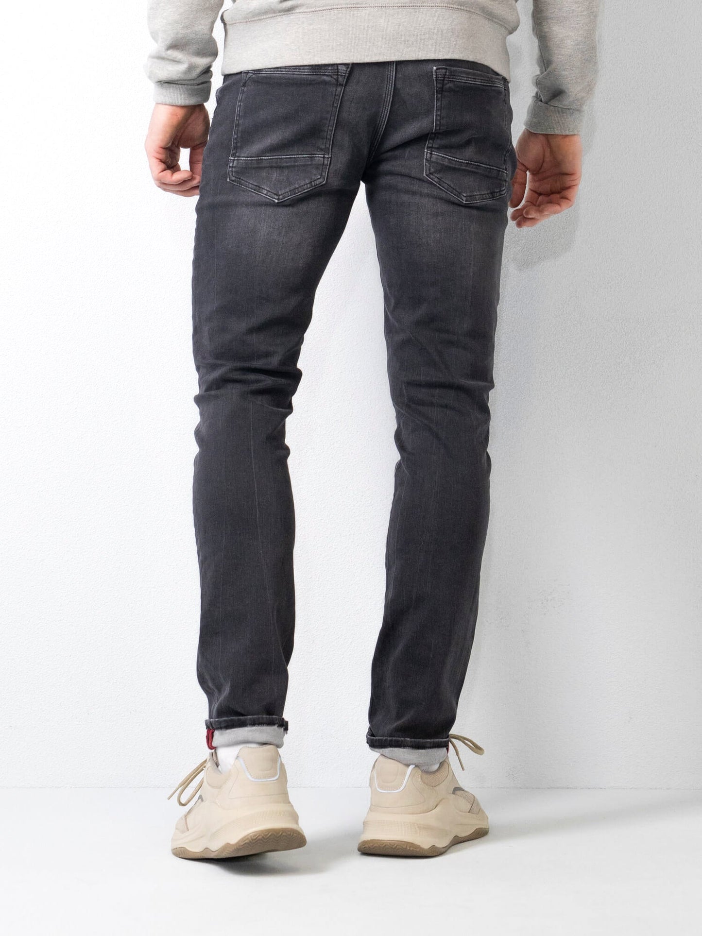 Jeans slim fit uomo, colore nero, indossati con sneakers bianche e felpa grigia. Moda casual maschile, abbigliamento moderno e confortevole.