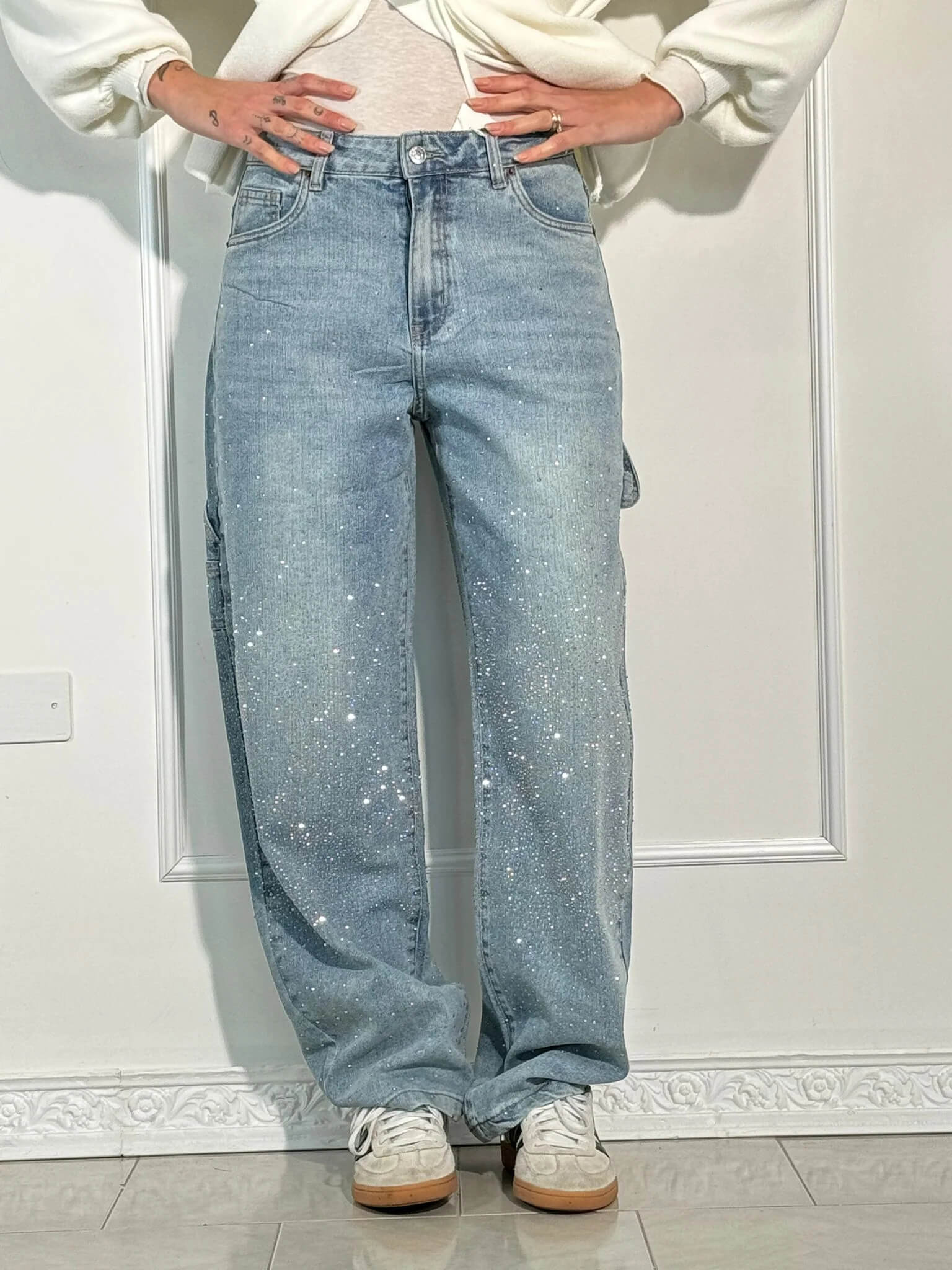 Jeans a gamba larga con paillettes scintillanti, indossati con sneakers bianche. Moda casual, stile trendy, abbigliamento femminile moderno.