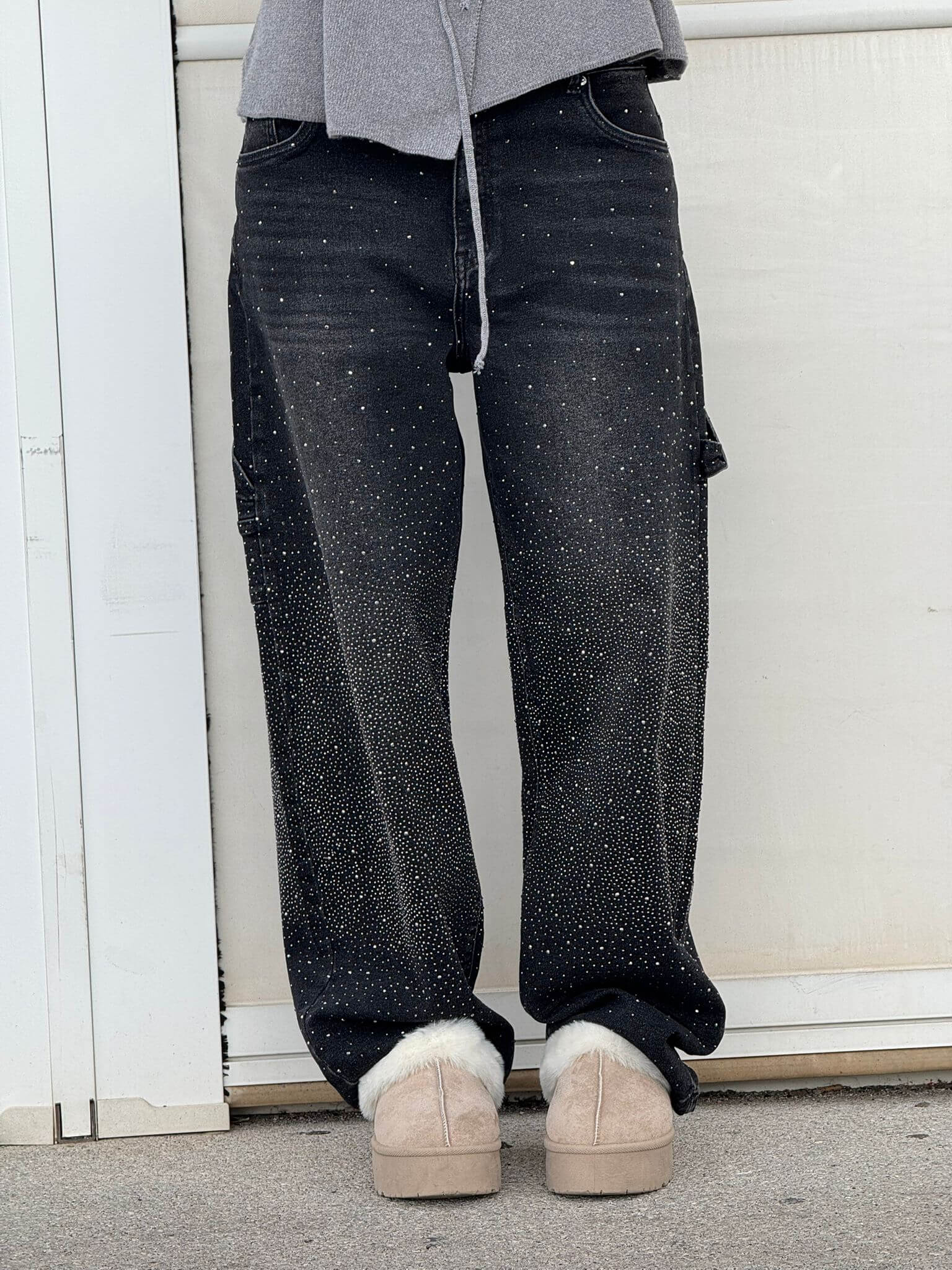 Jeans neri con dettagli scintillanti, indossati con scarpe beige invernali, su sfondo bianco. Moda casual, abbigliamento trendy, stile urbano.