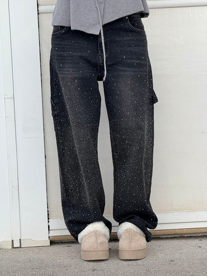 Jeans neri con dettagli scintillanti, indossati con scarpe beige invernali, su sfondo bianco. Moda casual, abbigliamento trendy, stile urbano.