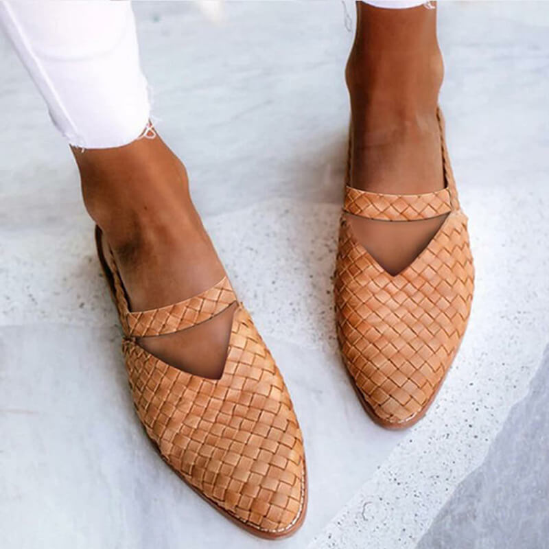 Scarpe intrecciate in pelle marrone chiaro su pavimento bianco, indossate con pantaloni bianchi. Scarpe estive eleganti, moda donna casual.