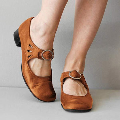 Scarpe Mary Jane in pelle marrone con tacco basso e cinturino con fibbia, indossate su pavimento grigio. Moda calzature donna eleganti e comode.