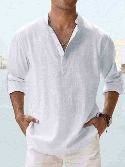 Camicia uomo bianca in lino, maniche lunghe arrotolate, collo alla coreana, stile casual estivo. Sfondo sfocato, look elegante e rilassato.