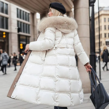 Donna con cappotto bianco imbottito e cappuccio in pelliccia, berretto nero, borsa in mano, cammina in città. Moda invernale elegante e chic.